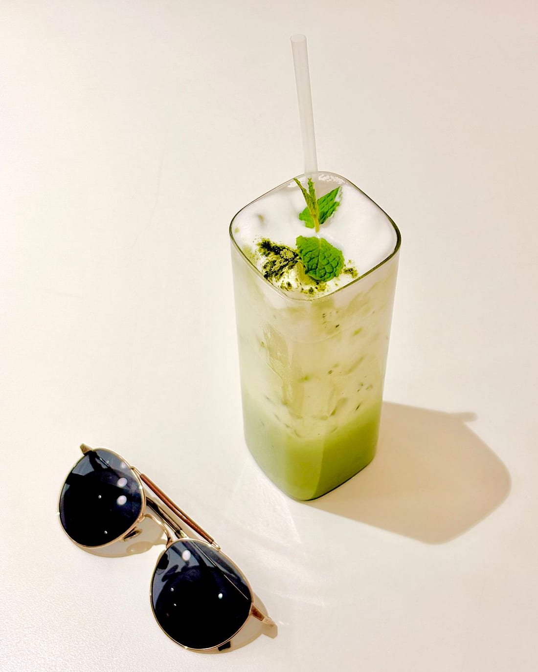 An iced matcha latte in a tall glass beside sunglasses on a sunlit table