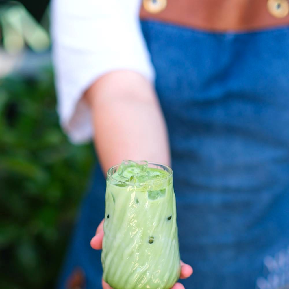 A hand holding an iced matcha latte from the Nalu matcha cart